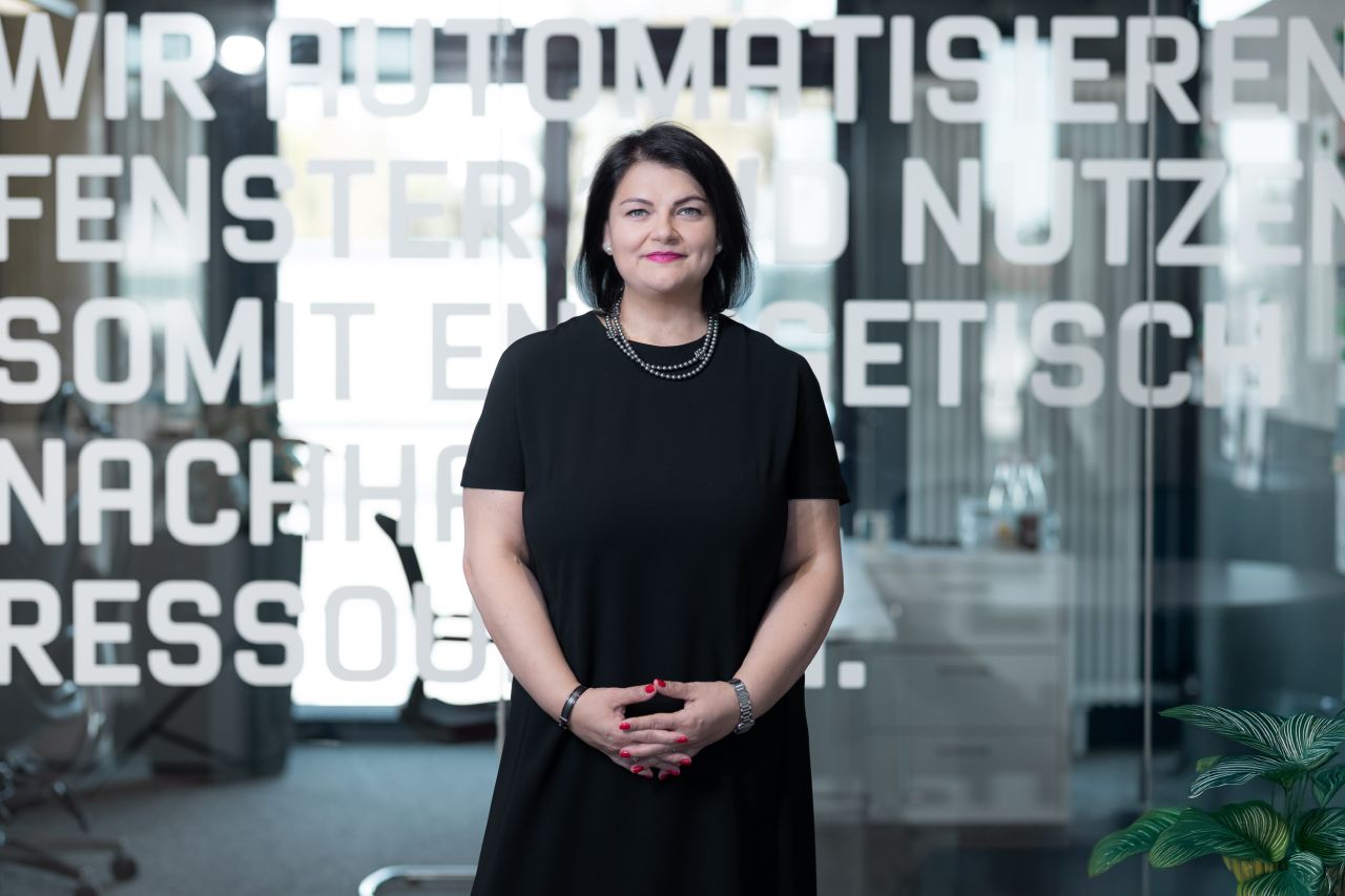 Ramona Meinzer im schwarzen Kleid vor einer Glaswand mit Leitsatz
